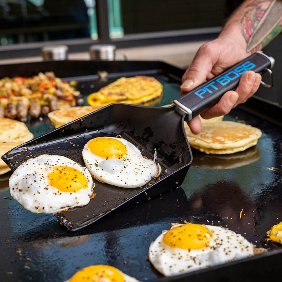 Ultimate griddle grub shovel scooping up 2 eggs on a griddle flat top