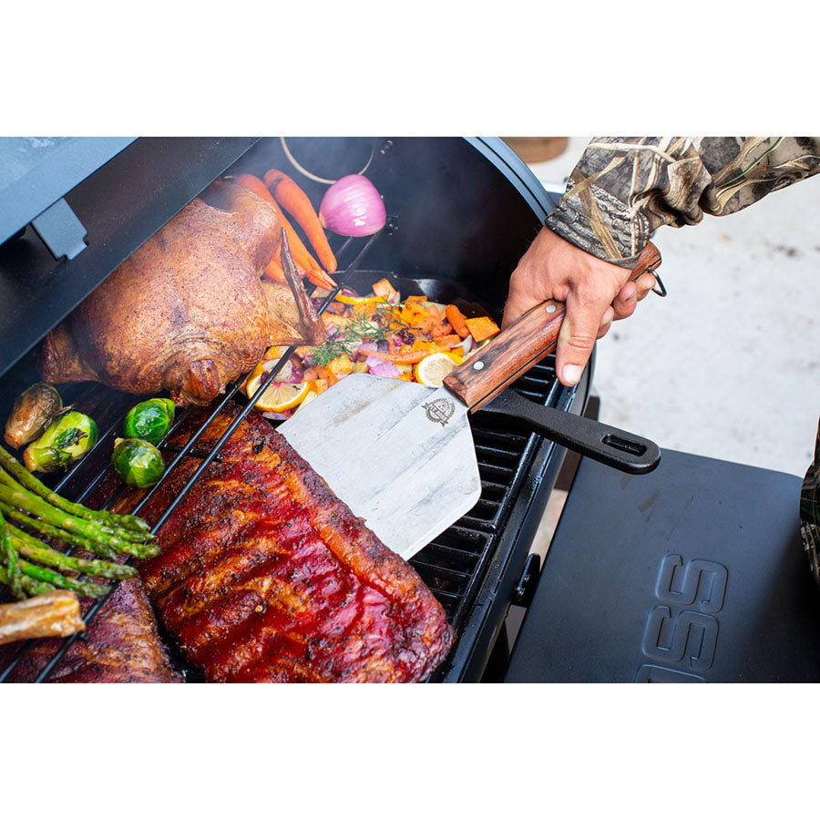 close up of food grilling on grill grates with large spatula flipping meat